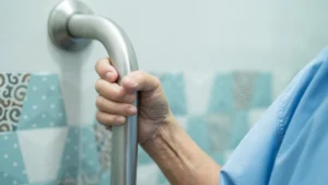 Close-up of an elderly person holding a stainless steel grab bar in a bathroom. Installing grab bars is a key tip for bathing elderly individuals safely at home.