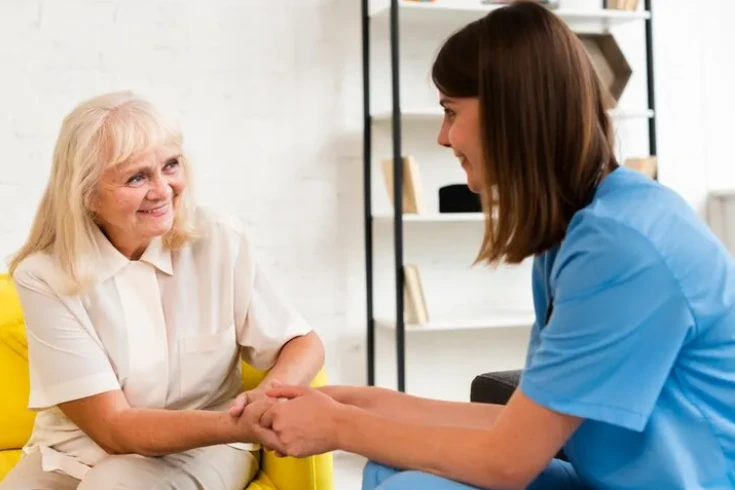 A caregiver from a home care agency holds hands with an elderly woman, providing emotional support and companionship in a warm and comfortable setting.