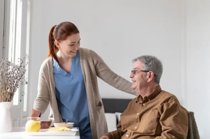 A caregiver from a home care agency smiles while assisting an elderly man during mealtime, ensuring proper nutrition and friendly companionship.