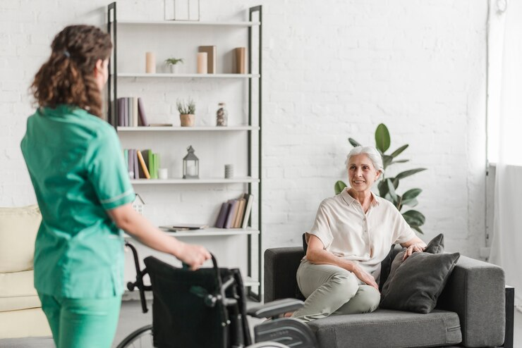 A caregiver from a home care agency approaches an elderly woman with a wheelchair, ready to assist with mobility support in a cozy home environment.