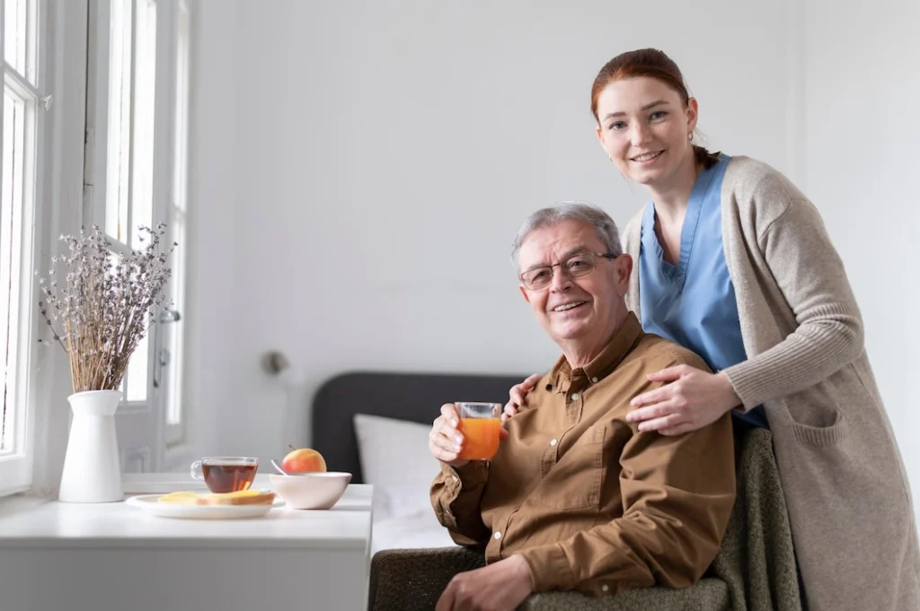 A happy elderly man enjoying a nutritious breakfast with orange juice, tea, toast, and fruit, accompanied by a caring nurse.